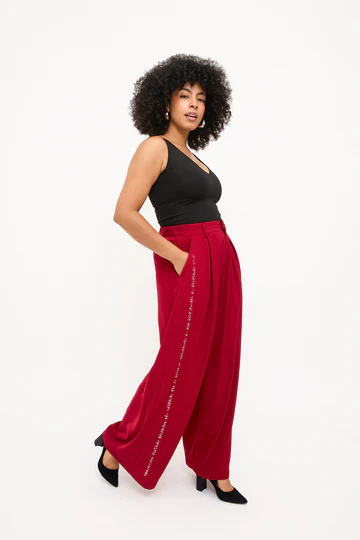 Woman wears red loose fitting trousers with braille in white vertically down the side seam